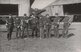 Vor einem Flugzeug stehen acht Männer in Uniform. Dahinter sind Hangars zu sehen.